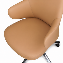 Close-up of a tan chair with a rounded seat, curved back and arms, visible stitching, and a partially visible silver-colored base with a black caster.