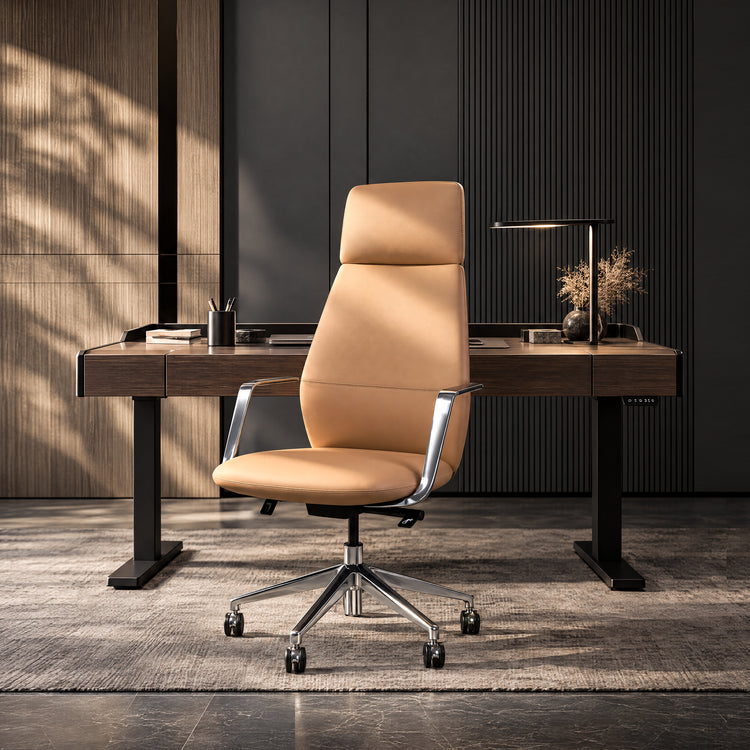 Tan high-back office chair with shiny armrests and a five-spoke wheeled base in front of a dark desk with a lamp, books and a vase of dried stems.