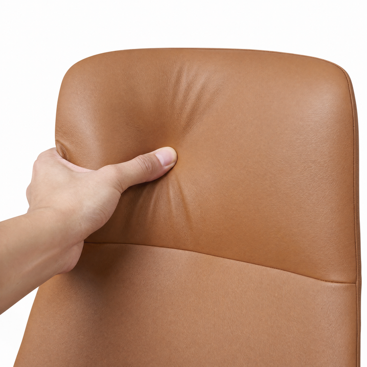 A hand presses into the tan upholstered backrest of a chair, creating a visible indentation.