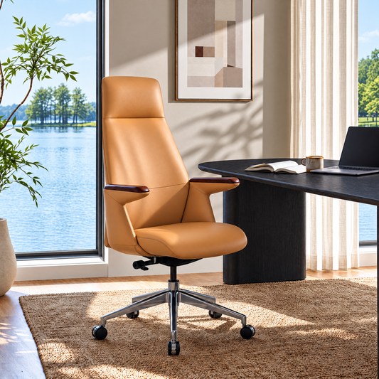 Tan high-back office chair with padded armrests and a five-spoke wheeled base beside a dark desk with a laptop, open book and mug, near windows overlooking water and trees.