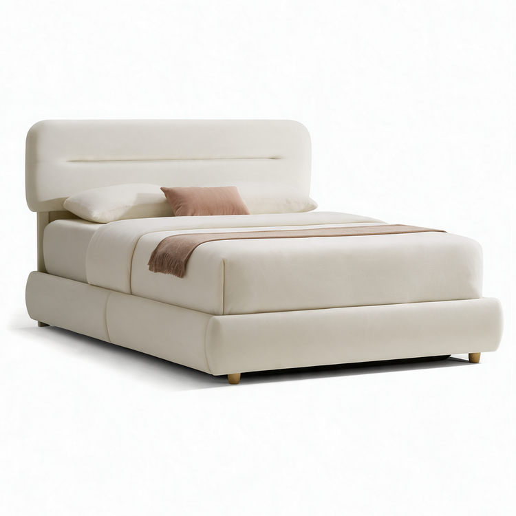 Cream-colored bed with a rounded rectangular headboard, padded frame, short legs, white bedding, a pink accent pillow and a fringed brown throw across the foot.