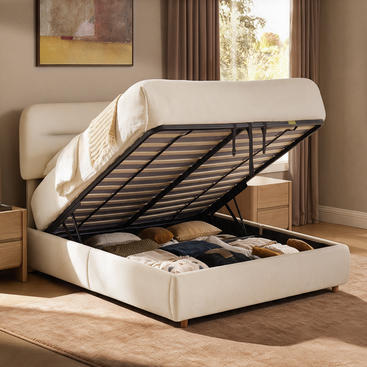 Cream upholstered bed with its mattress and slatted base lifted to reveal an under-bed compartment filled with cushions and blankets.