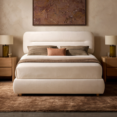 Cream upholstered bed with a rounded headboard, brown pillows and throw, flanked by bedside cabinets and lamps beneath a brown abstract painting.