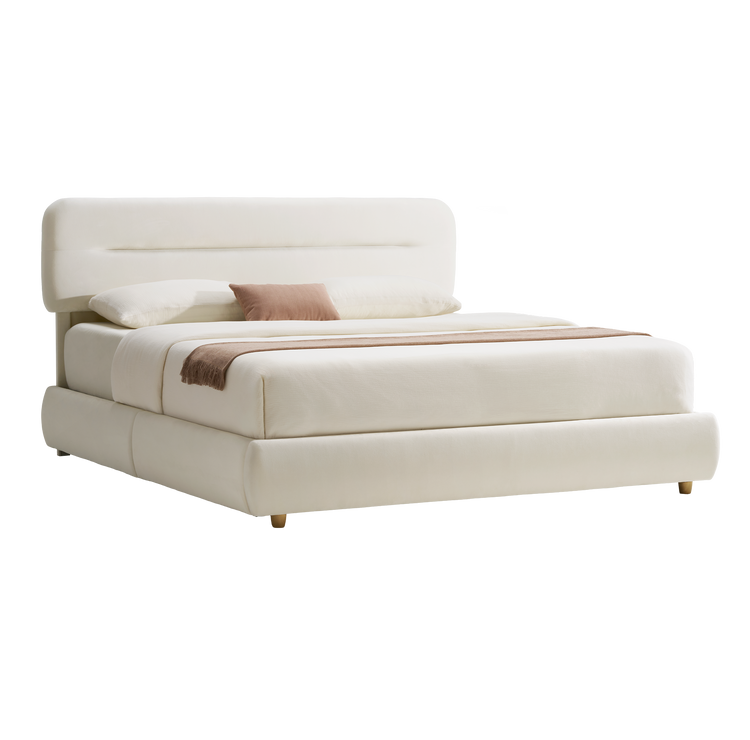 Cream upholstered bed with a rounded rectangular headboard, short tapered feet, white bedding, a pink accent pillow and a brown fringed throw across the foot.