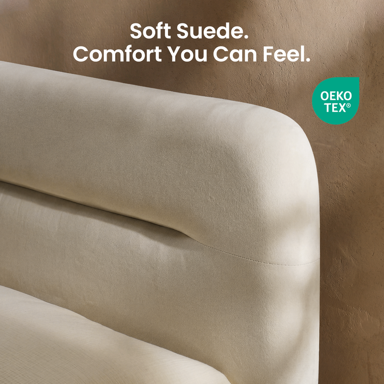 Close-up of a cream upholstered headboard with a rounded top edge and curved horizontal seam against a textured brown wall.