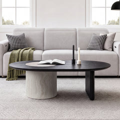 Dark oval coffee table with a pale circular inset and contrasting cylindrical support in front of a white sofa