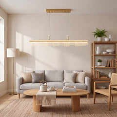 A long illuminated pendant with layered perforated panels hangs above a gray sofa and oval coffee table, with a floor lamp on the left and open shelving on the right.