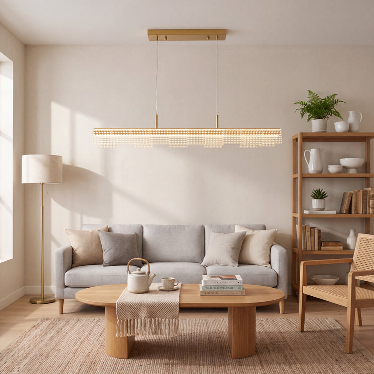 A long illuminated pendant with layered perforated panels hangs above a gray sofa and oval coffee table, with a floor lamp on the left and open shelving on the right.