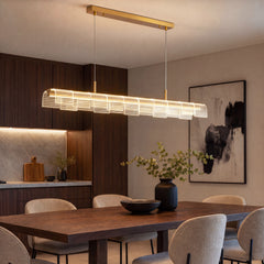 An illuminated linear pendant with gold-colored fittings and overlapping dotted panels hangs above a dark dining table surrounded by beige chairs.