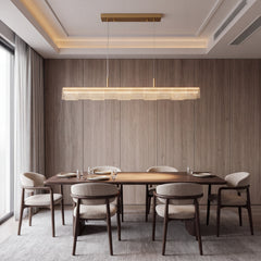 A long illuminated pendant with rows of bright dots hangs over a dining table set with plates and glasses, surrounded by six upholstered chairs against a paneled wall.