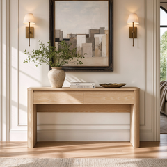 Slim light wood console table with two shallow drawers stands beneath framed wall art