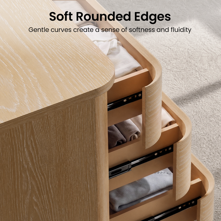 Close-up of a pale wood drawer unit with rounded corners, three partially open drawers, and folded fabric inside