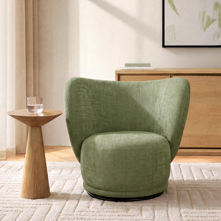 Green wraparound chair is paired with a small wood-grain pedestal table holding a clear glass