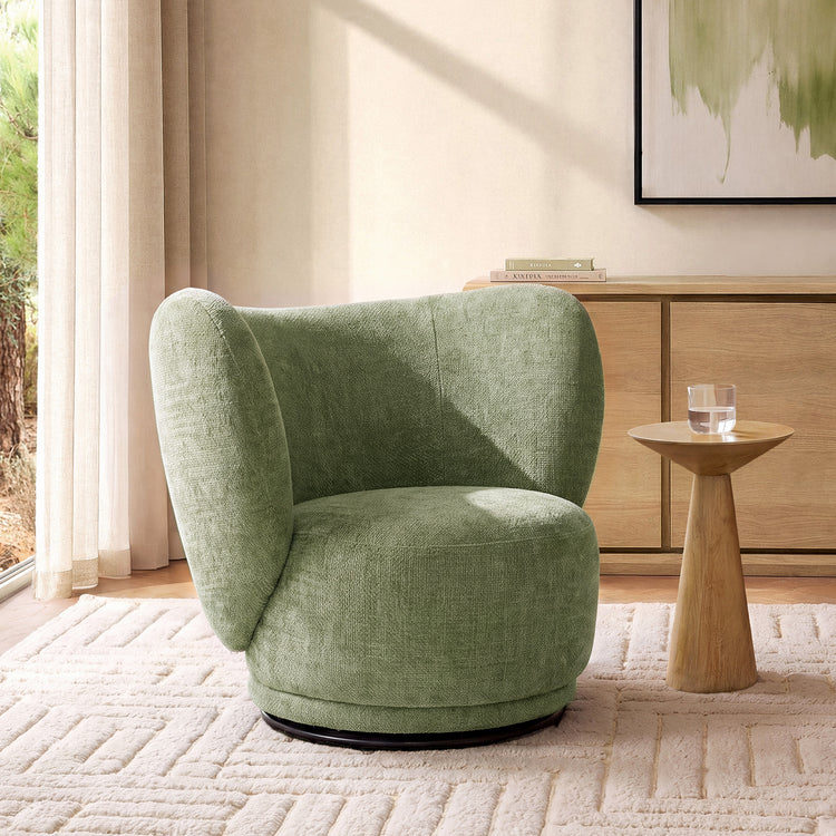 A sage-green wraparound chair stands beside a pedestal table in a sunlit neutral room