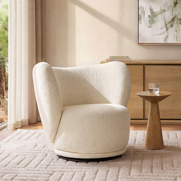 Cream wraparound chair stands beside a tapered pedestal table holding a clear drinking glass