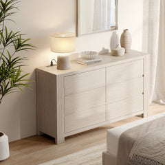 Light wood six-drawer dresser with decor on top beside a bed in a bright bedroom