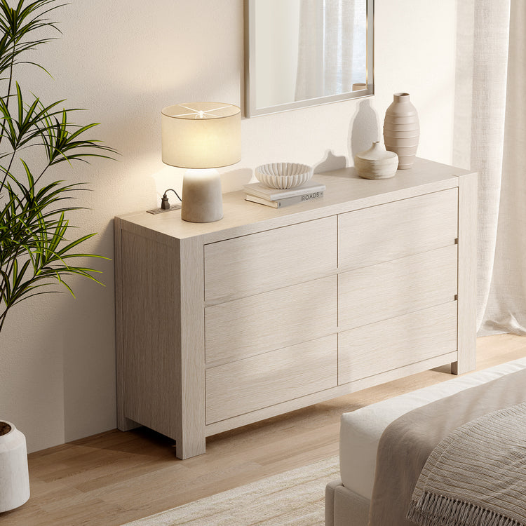 Light wood six-drawer dresser with decor on top beside a bed in a bright bedroom