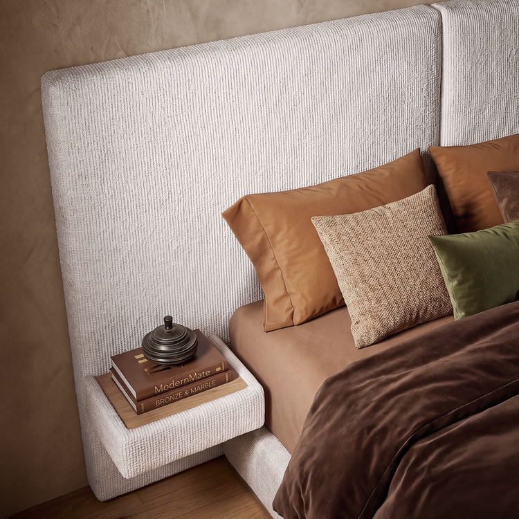 Close bedroom view of a tall cream upholstered headboard, brown bedding, pillows, and a small bedside shelf