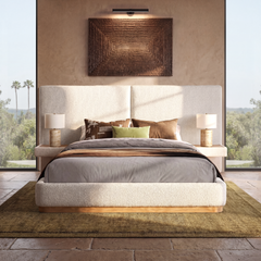 Cream upholstered bed with brown bedding centered between two bedside lamps below dark wall art