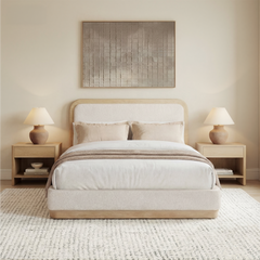A cream upholstered bed with a tall rounded headboard is centered between matching wood nightstands and lamps