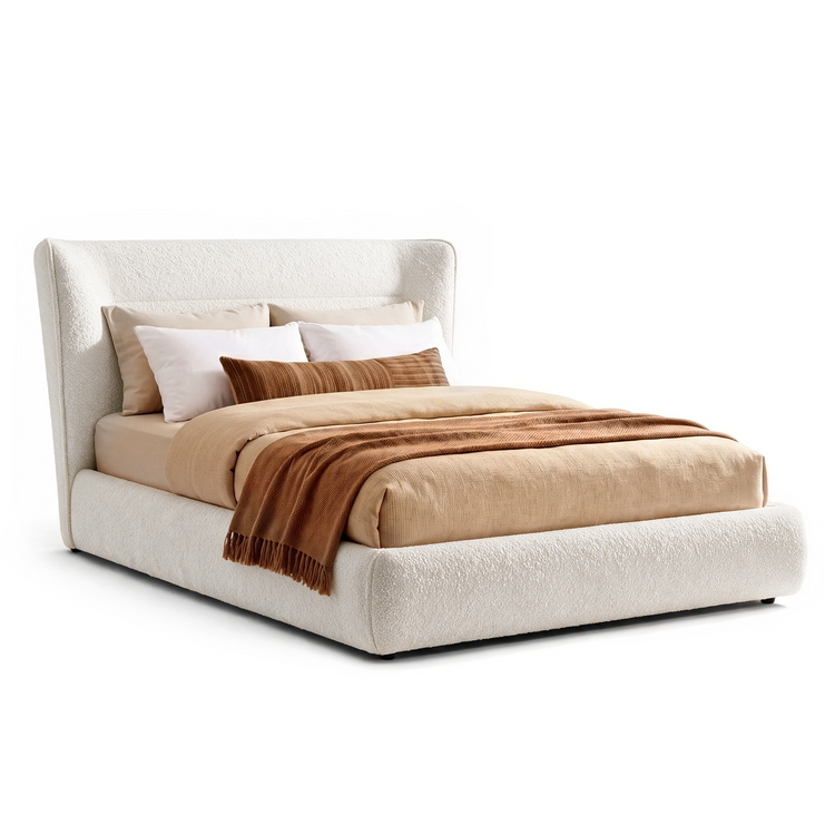 Cream upholstered bed with a tall winged headboard and rounded footboard, dressed in beige bedding, white and beige pillows, a brown striped cushion and a brown fringed throw.