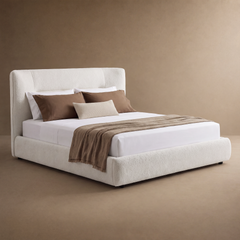 Cream upholstered bed with a tall padded headboard, white bedding, brown pillows, a small ribbed cream cushion and a brown throw draped across the foot.