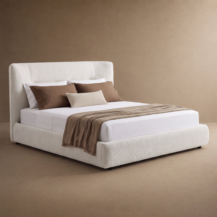 Cream upholstered bed with a tall padded headboard, white bedding, brown pillows, a small ribbed cream cushion and a brown throw draped across the foot.