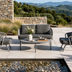 Dark outdoor sofa, two lounge chairs, and a low coffee table arranged on a sunny stone patio