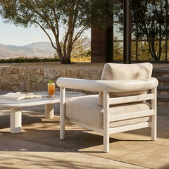 Light cushioned lounge chair with a rounded tubular frame sits beside a low round table outdoors