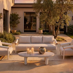 Light outdoor sofa and chairs arranged around an oval coffee table on a patio at dusk