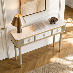 A three-drawer console has a white veined top, ribbed legs, patterned fronts, and warm-metal trim