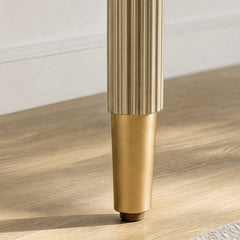 Close-up of a fluted gold-toned furniture leg ending in a smooth brass-colored foot