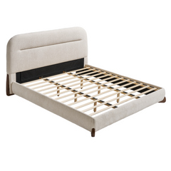 Cream upholstered bed frame with a tall, rounded headboard, a horizontal recessed seam, exposed pale slats, and short dark brown legs, shown without a mattress.