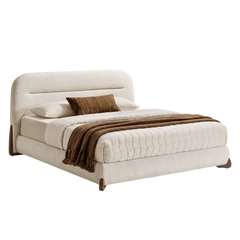 Cream upholstered bed with a rounded rectangular headboard and brown feet, dressed in cream quilted bedding, white pillows, a brown accent cushion and a brown tasseled throw.