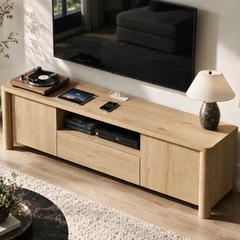 A light wood media console beneath a wall-mounted television, with a turntable, tablet, charging devices, books, and a table lamp.