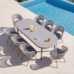 Gray woven chairs surround a large outdoor dining table, Dining set stands beside a swimming pool