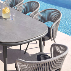 An oval gray dining table and four woven-back chairs are arranged beside a swimming pool