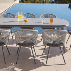 Gray outdoor dining table is surrounded by woven-back chairs beside a pool