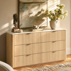Light wood six-drawer dresser is styled with flowers, books, and sculpture