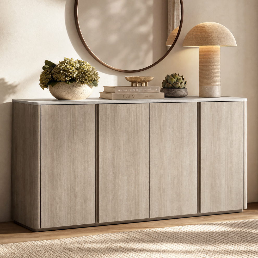 Light wood four-door sideboard with decor and lamps beneath a round mirror