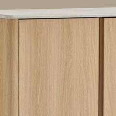 Close-up shows pale wood-grain cabinet fronts beneath a rounded, lightly veined white top