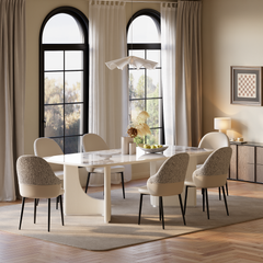 Dining room with a white patterned table, six cream and gray chairs, a sculptural pendant light, and tall arched windows framed by curtains.