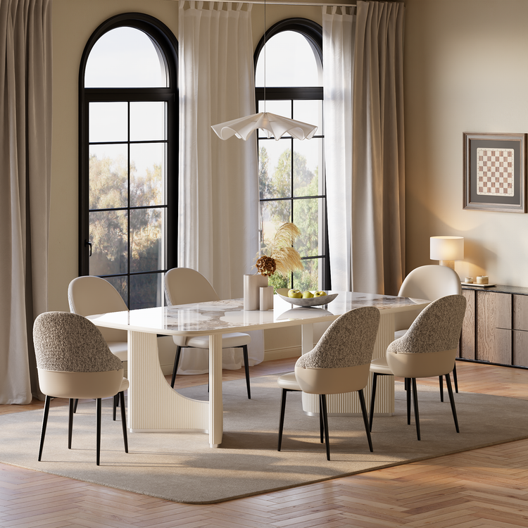Dining room with a white patterned table, six cream and gray chairs, a sculptural pendant light, and tall arched windows framed by curtains.