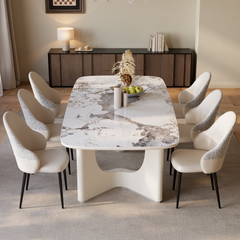 A dining room with a long white-and-gray veined table, six upholstered chairs, and a dark wooden sideboard against the back wall.