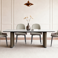 White-top dining table with dark edging and brown pedestal supports surrounded by light upholstered chairs