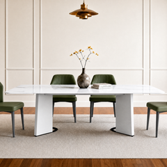 White veined dining table with broad angular pedestal legs and green chairs beneath a pendant light