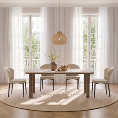 Pale rectangular dining table with wood-tone legs and four cream chairs in front of tall curtained windows