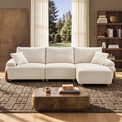 Cream sofa with three back cushions, two throw pillows and a matching ottoman in front of the right seat, set on a patterned rug beside a low coffee table.