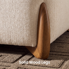Close-up of a rounded brown furniture leg with visible grain beside cream ribbed upholstery, resting on a textured geometric rug.