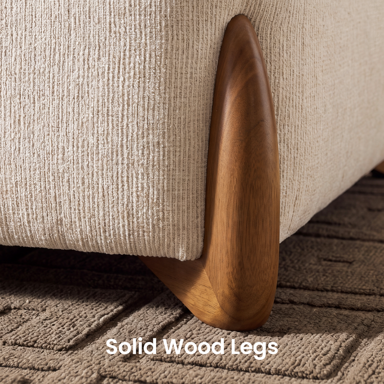 Close-up of a rounded brown furniture leg with visible grain beside cream ribbed upholstery, resting on a textured geometric rug.